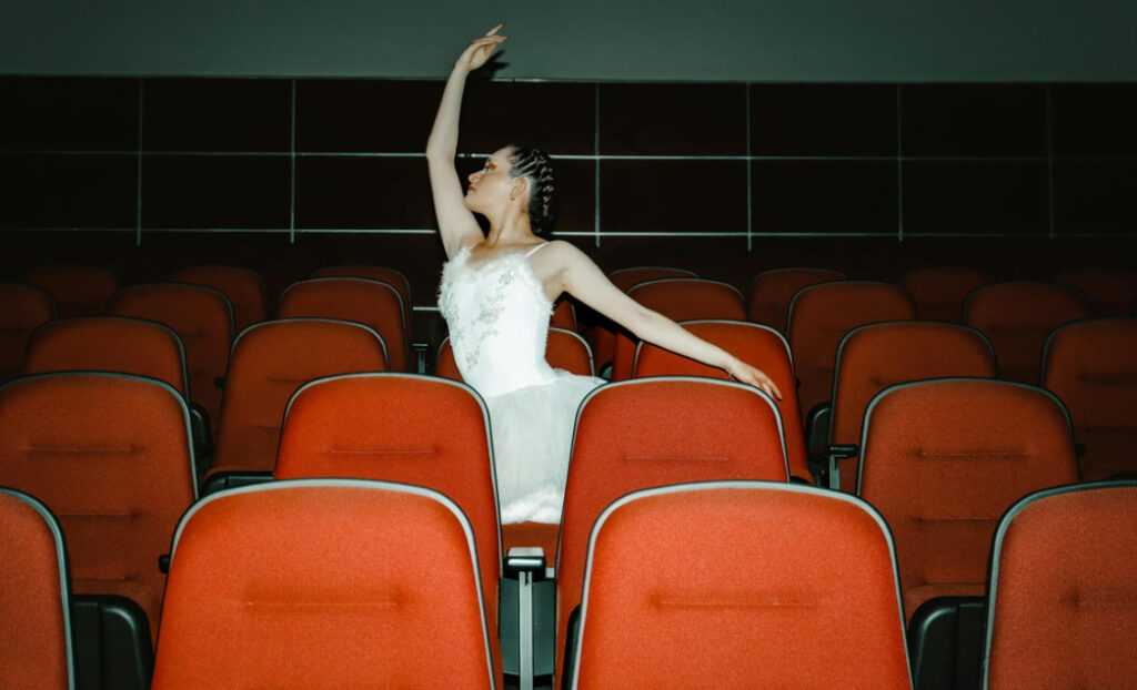 Ballerina reaching up in an empty theater with red seats