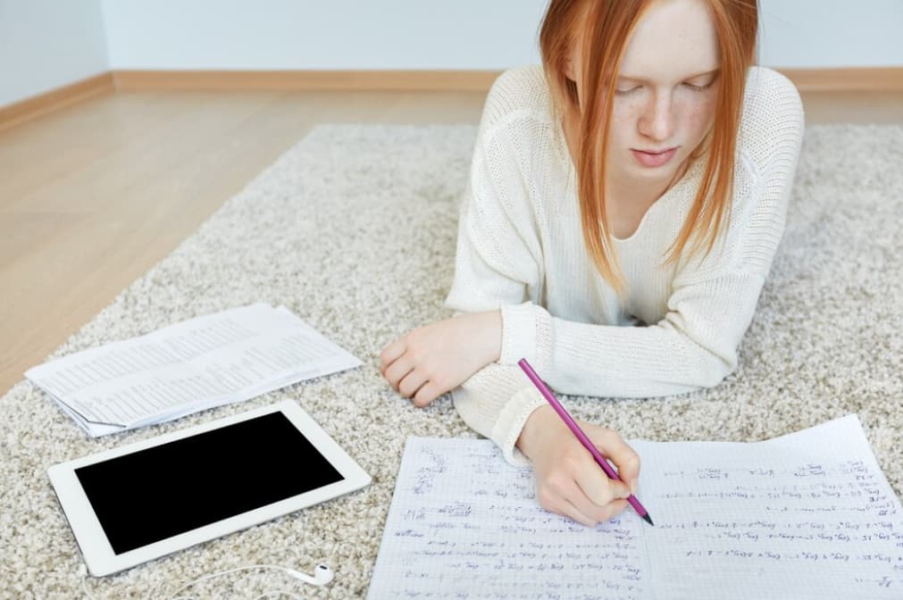 A student writing notes while studying on the floor