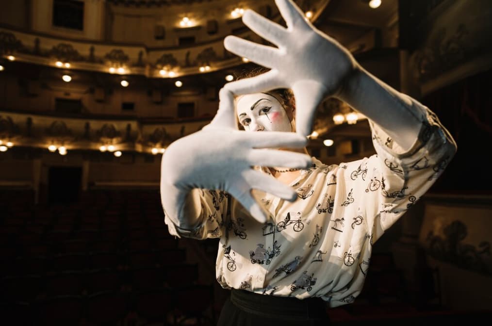 Mime artist framing a face with hands in a theater auditorium