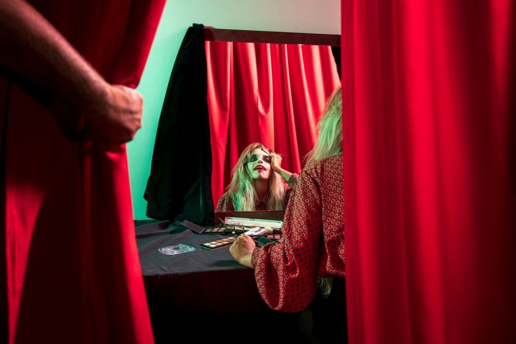Woman applying makeup behind red stage curtains